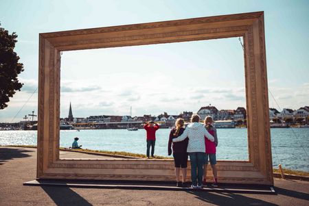 Familie macht ein Foto bei einem großen goldenen Bilderrahmen am Priwall